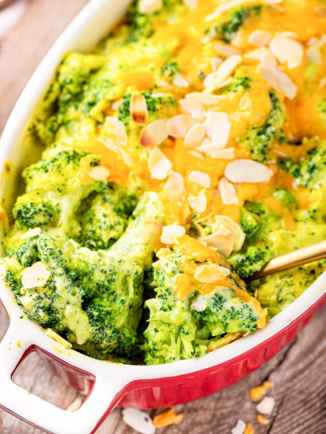 Broccoli florets covered in cheese about to be served from a casserole dish with a golden spoon.