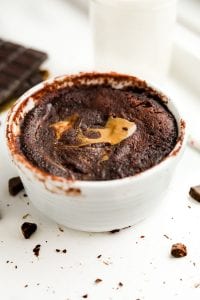 A chocolate cake with peanut butter in a white mug with a glass of milk behind it.