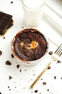 A chocolate mug cake on a white table next to a fork and a glass of milk.