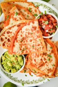 Cheddar cheese quesadillas cut up and stacked on top of each other on a white plate.