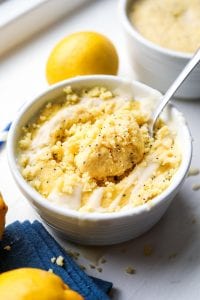 A lemon poppy seed mug cake covered in a glaze and a fork about to pull a piece of the cake from the mug.