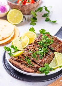 Cooked Flank steak cut up on a plate, and covered in chimichurri sauce.