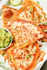 Quesadillas next to sides of tomato and guacamole.