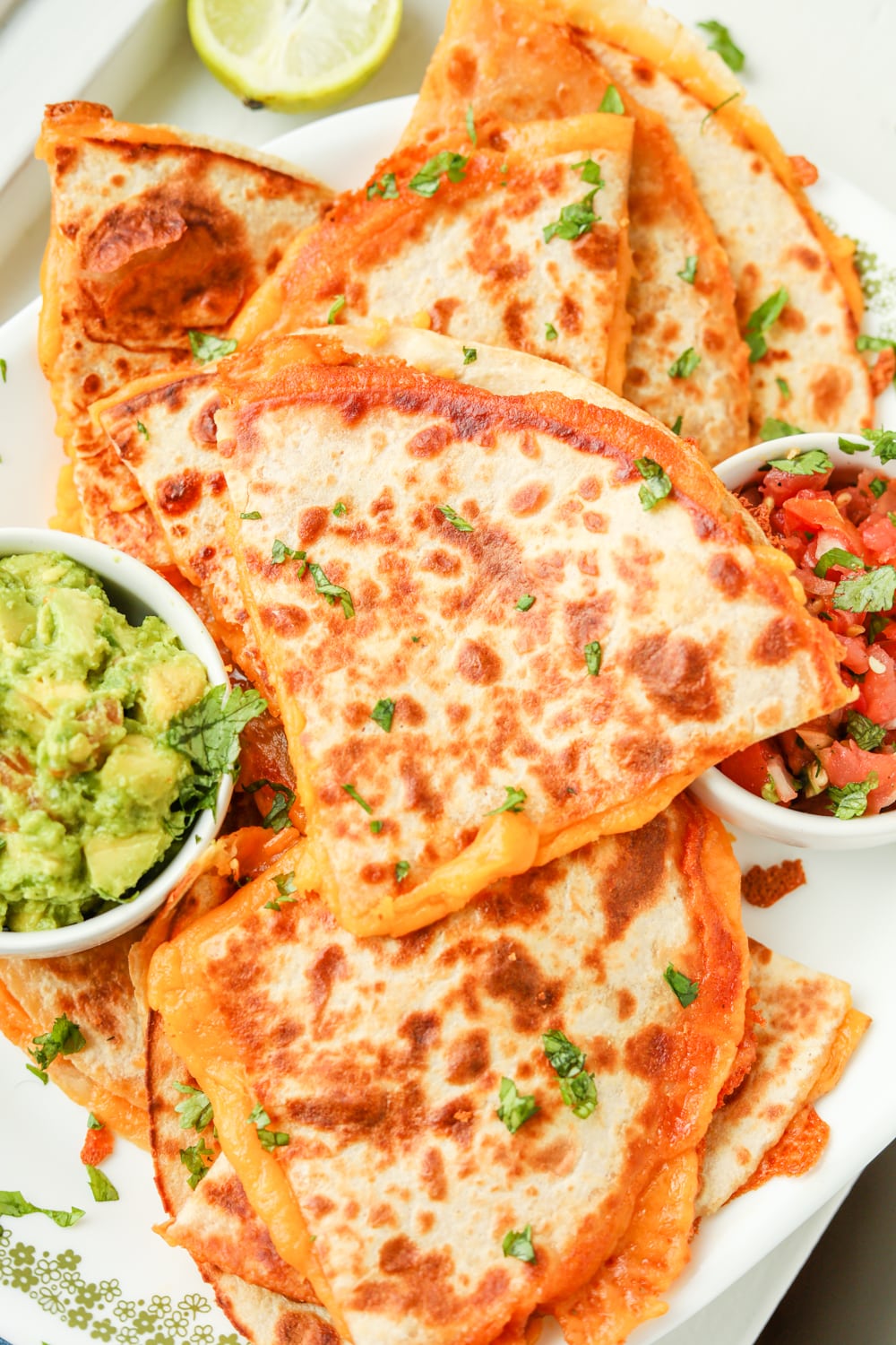 Quesadillas next to sides of tomato and guacamole.