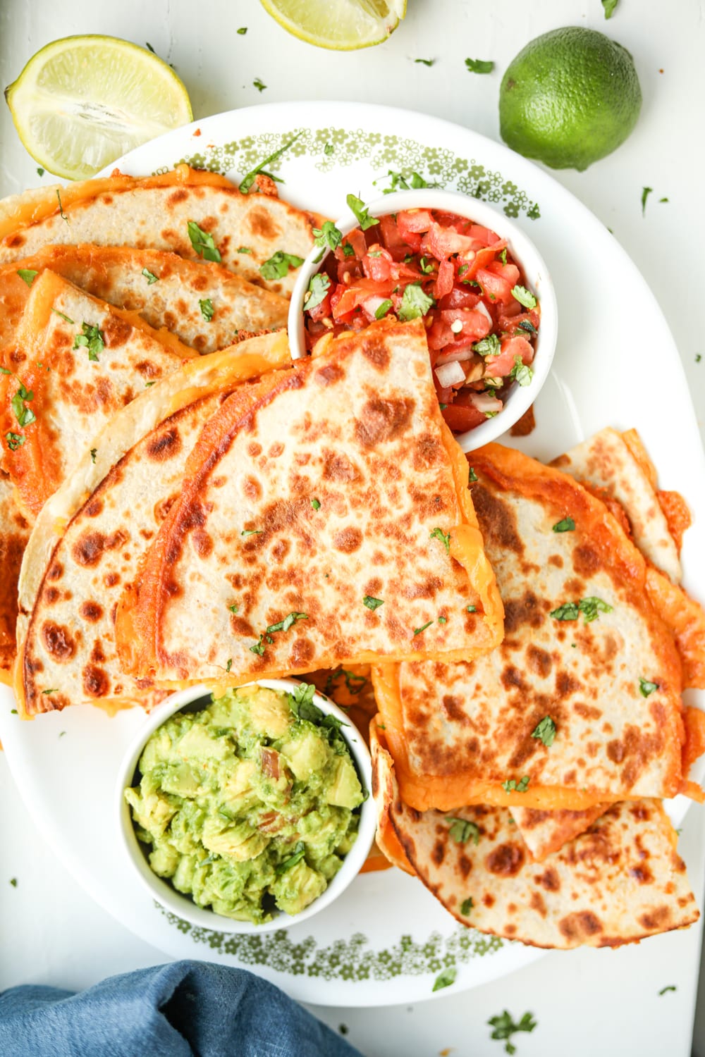 Quesadillas on a platter next to avocado and salsa.