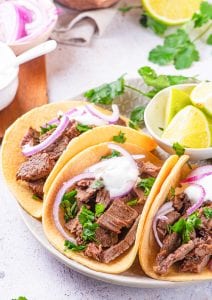 Carne Asada tacos topped with chimichurri sauce, red onions, and sour cream.