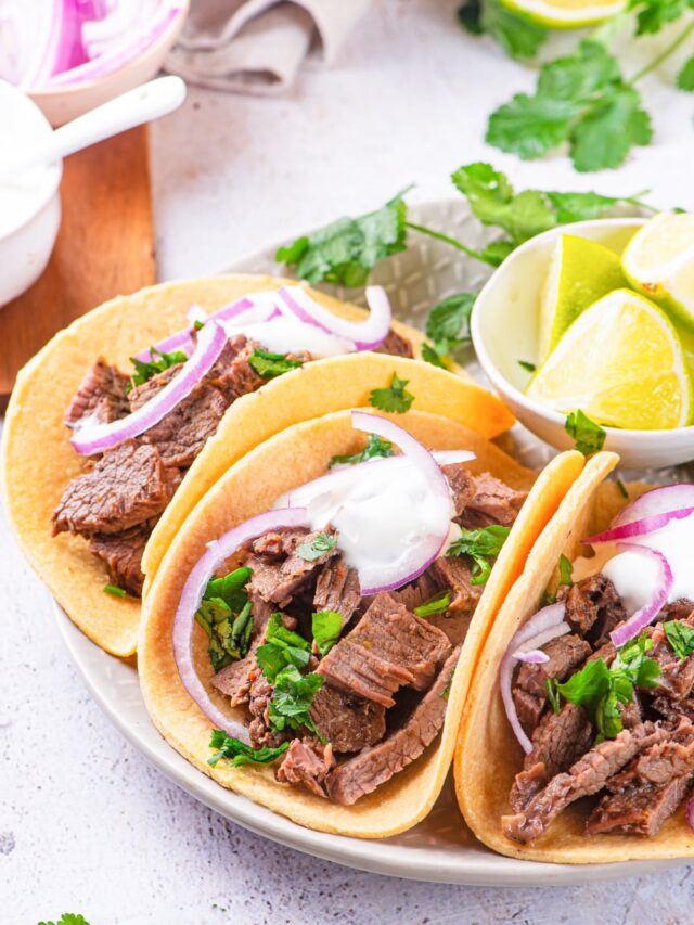 Carne Asada tacos topped with chimichurri sauce, red onions, and sour cream.