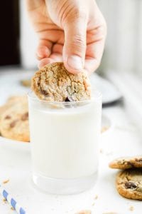 A chocolate chip cookie being dipped in a glass of milk.