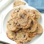 Chocolate chip cookies staked on top of each other on a white plate, next to a blue napkin.