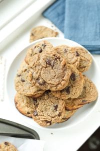 Chocolate chip cookies staked on top of each other on a white plate, next to a blue napkin.