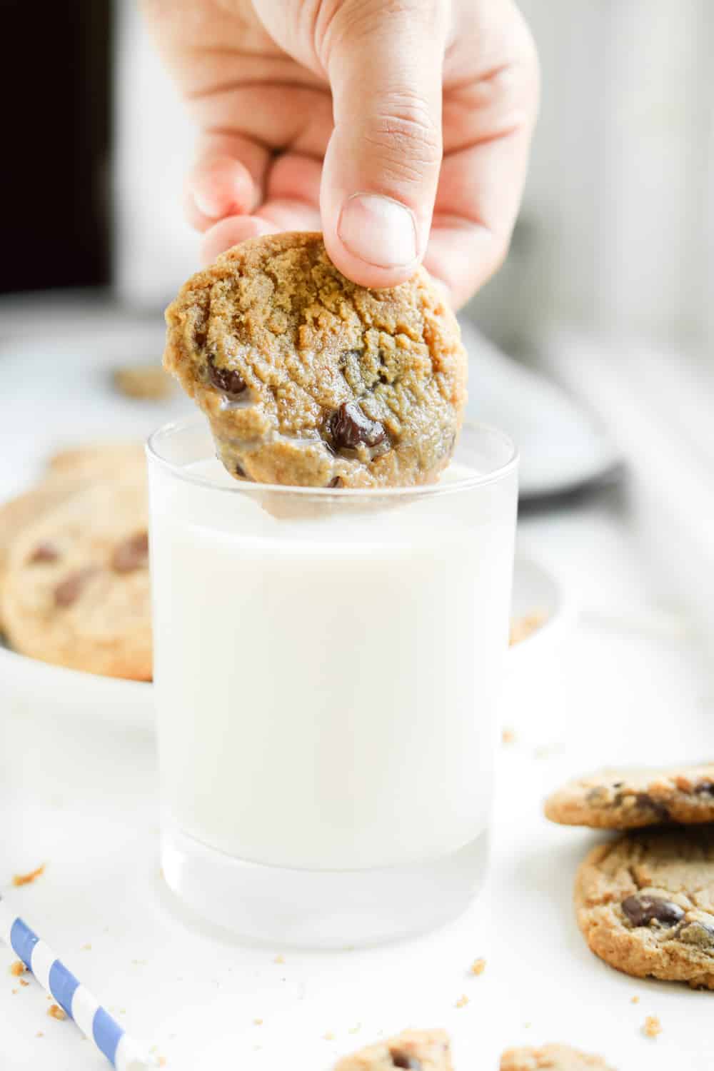 A glass of milk with a chocolate chip cookie about to be dipped in it.