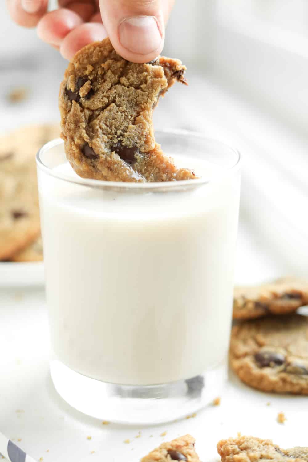 A chocolate chip cookie with a bite taken out of it being dipped into a glass of milk.