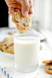 A chocolate chip cookie about to be dipped into a glass of milk.