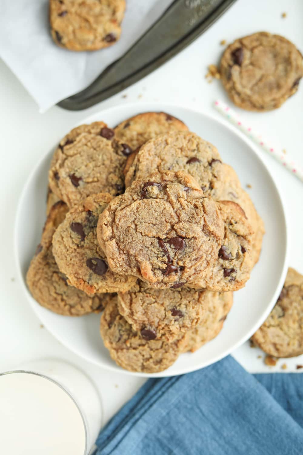 Chocolate chip cookies on a white plate, next to a glass of milk and a blue napkin.