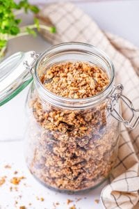 Granola in a glass jar on a white table.