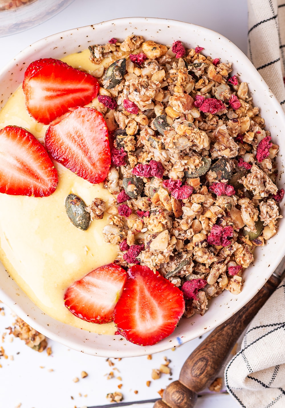 A bowl of yogurt with sliced up strawberries and granola in it.