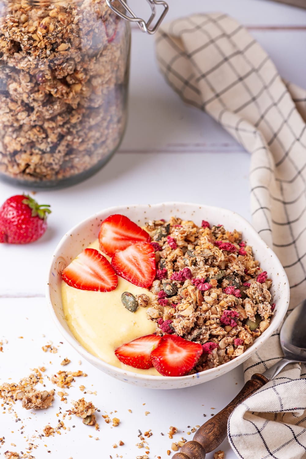 Granola and yogurt in a white bowl with cut-up strawberries on top.