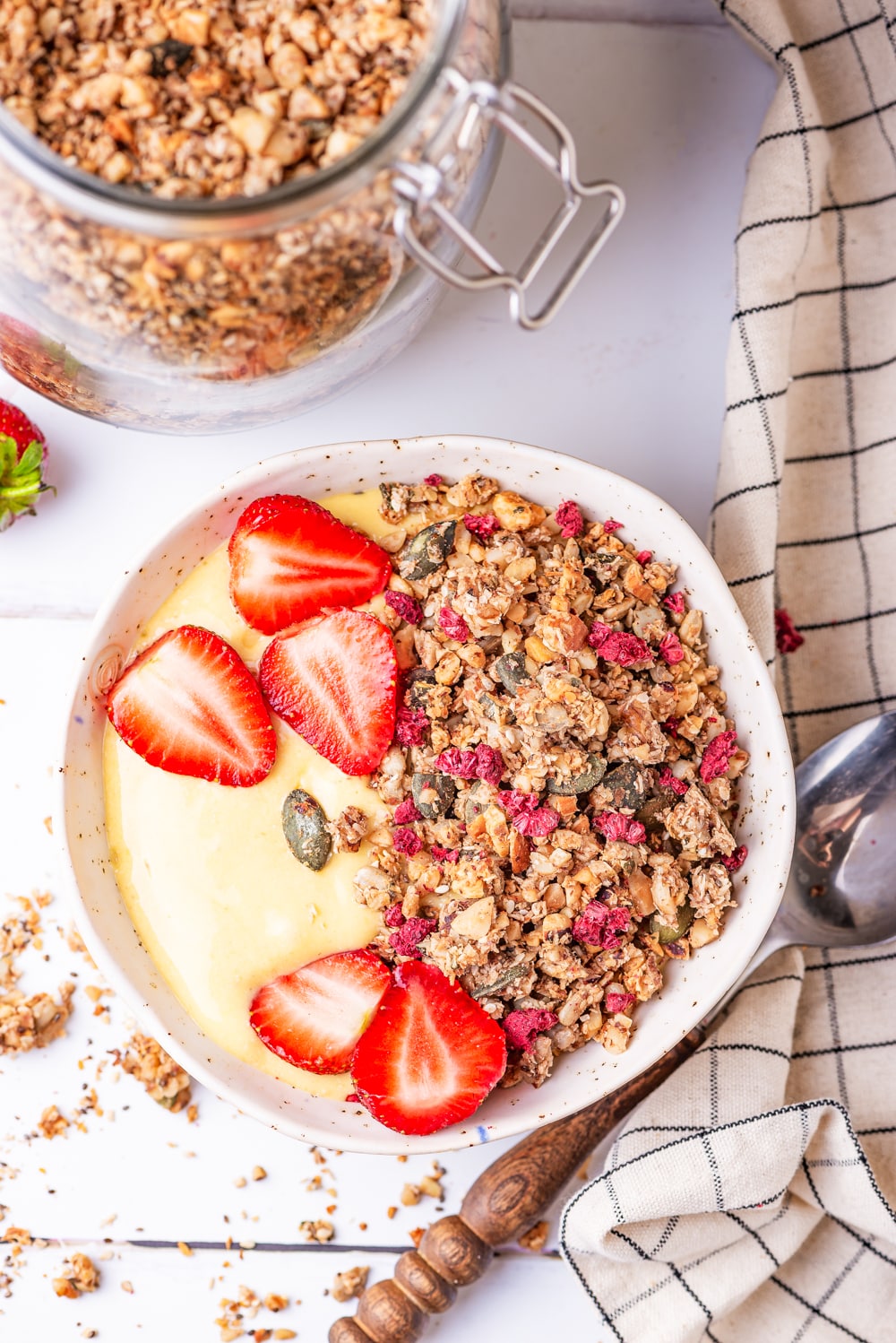 Granola, yogurt, and strawberries in a white bowl with a jar of granola next to it.