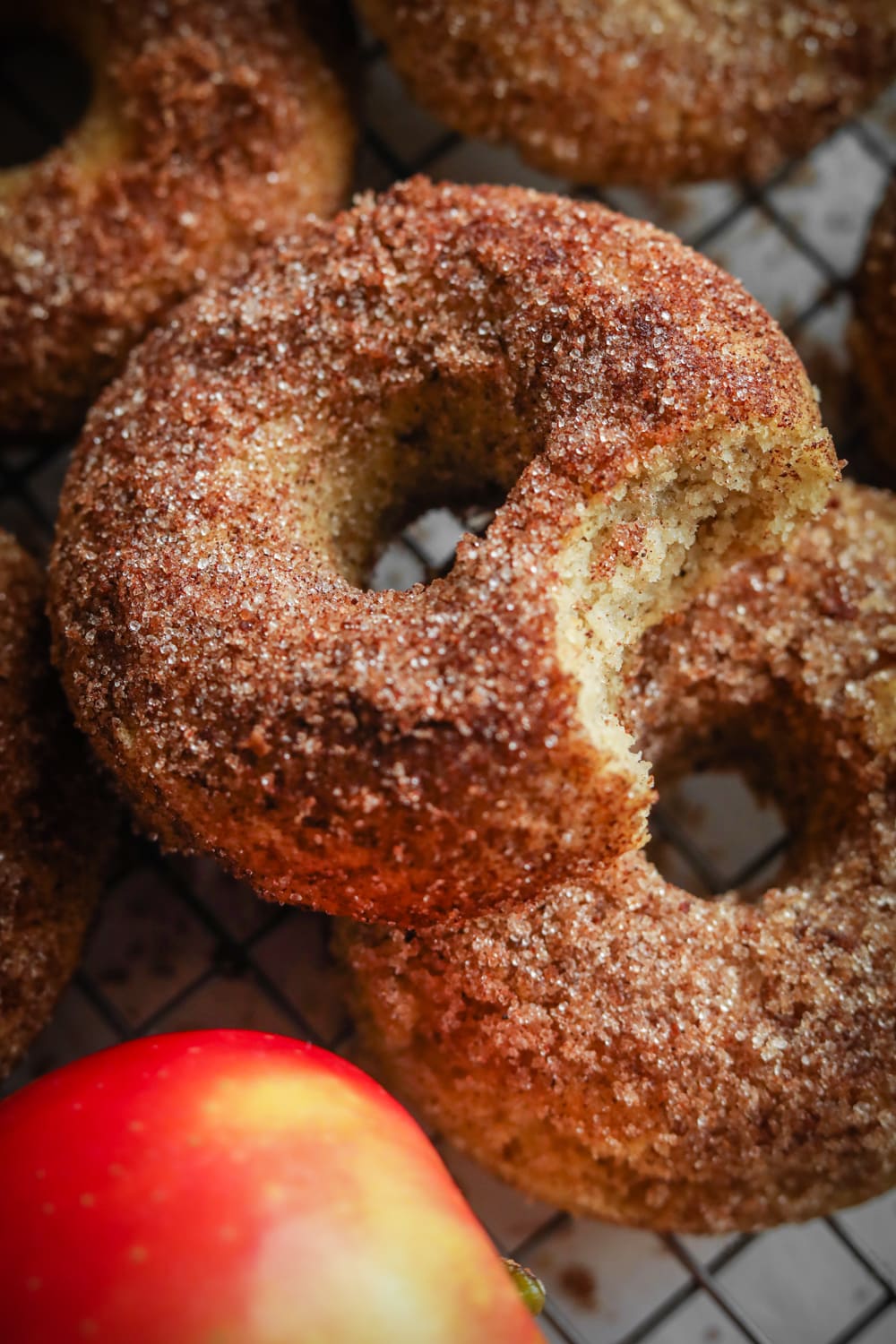 A donut with a bite taken out of it on top of another donut, and an apple in front of them.