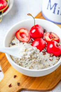 Oatmeal in a bowl with a white spoon taking some out.