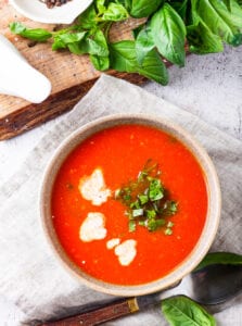 A bowl filled with tomato soup, heavy cream, and chopped basil.