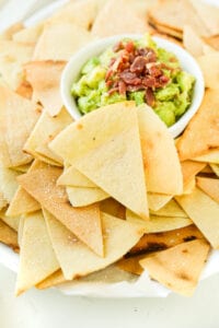 The side of a white platter that's full of tortilla chips and guacamole