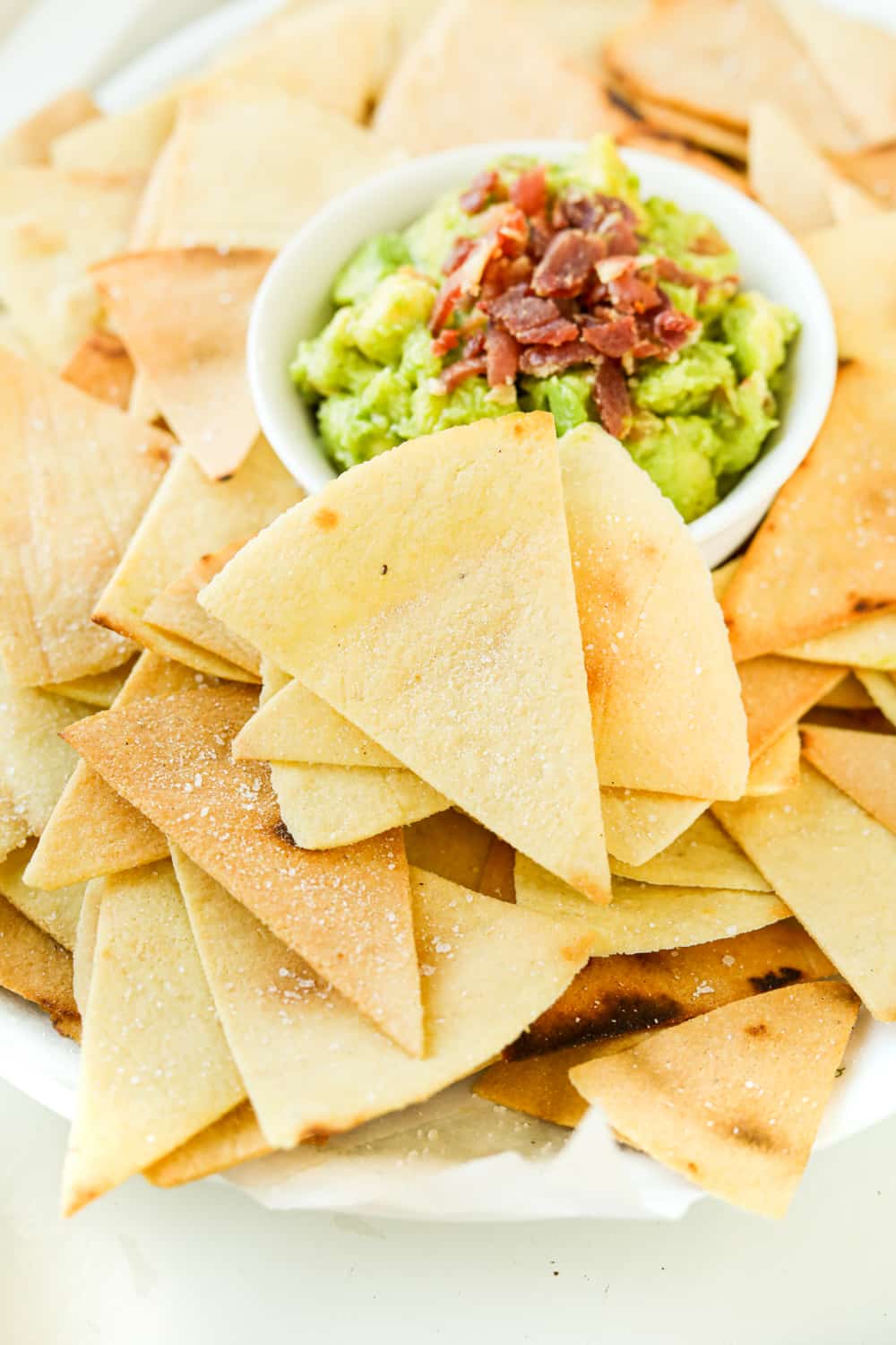 The side of a white platter that's full of tortilla chips and guacamole