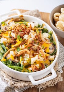 A white casserole dish filled with green beans, mushrooms, melted cheese, crispy onions, and pork rinds.