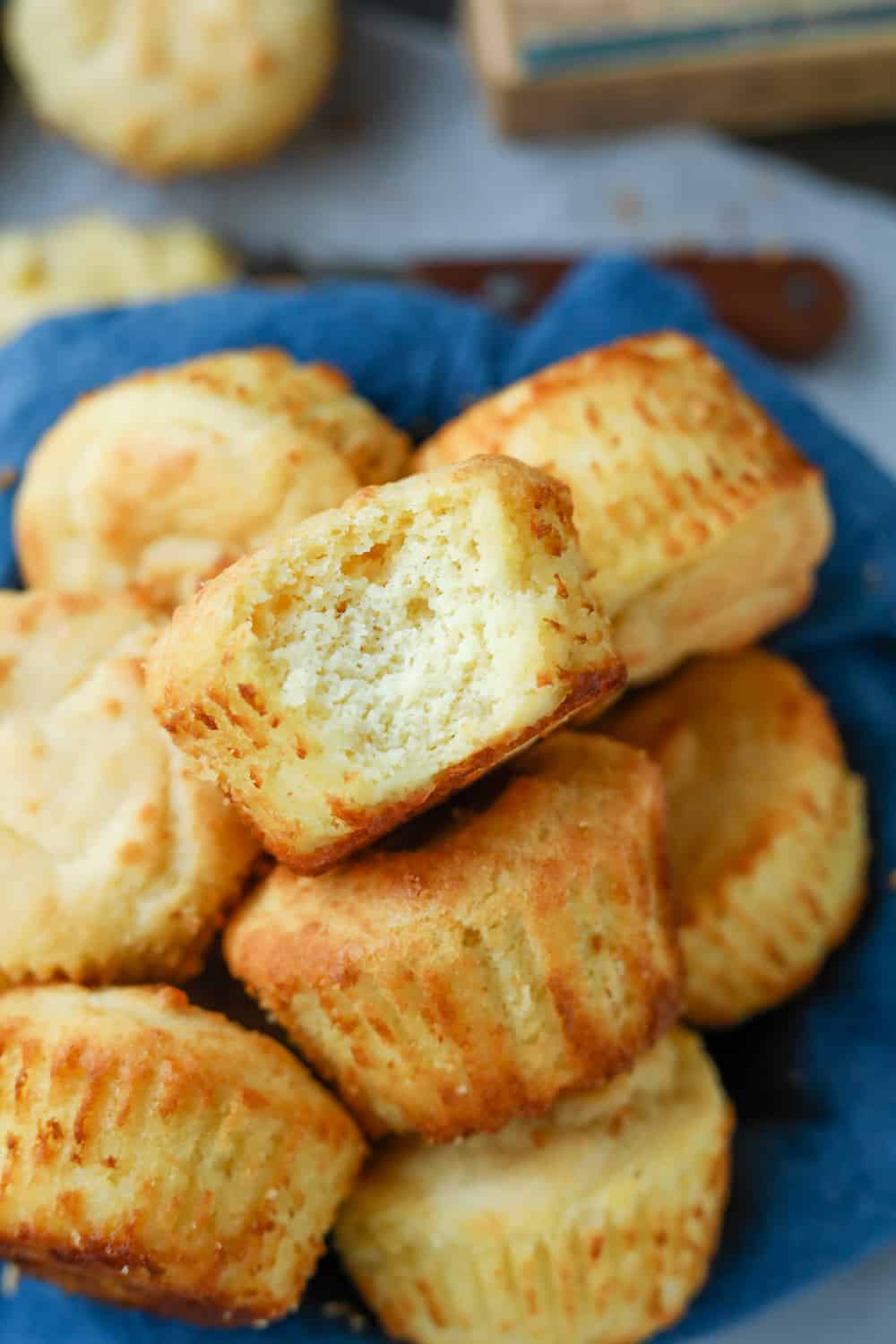 A biscuit with a bite missing thats placed on top of other biscuits with a blue towel underneath them.