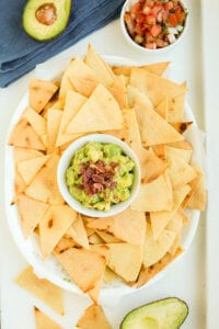 A white platter filled with tortilla chips with a small white bowl of guacamole in the middle of it.