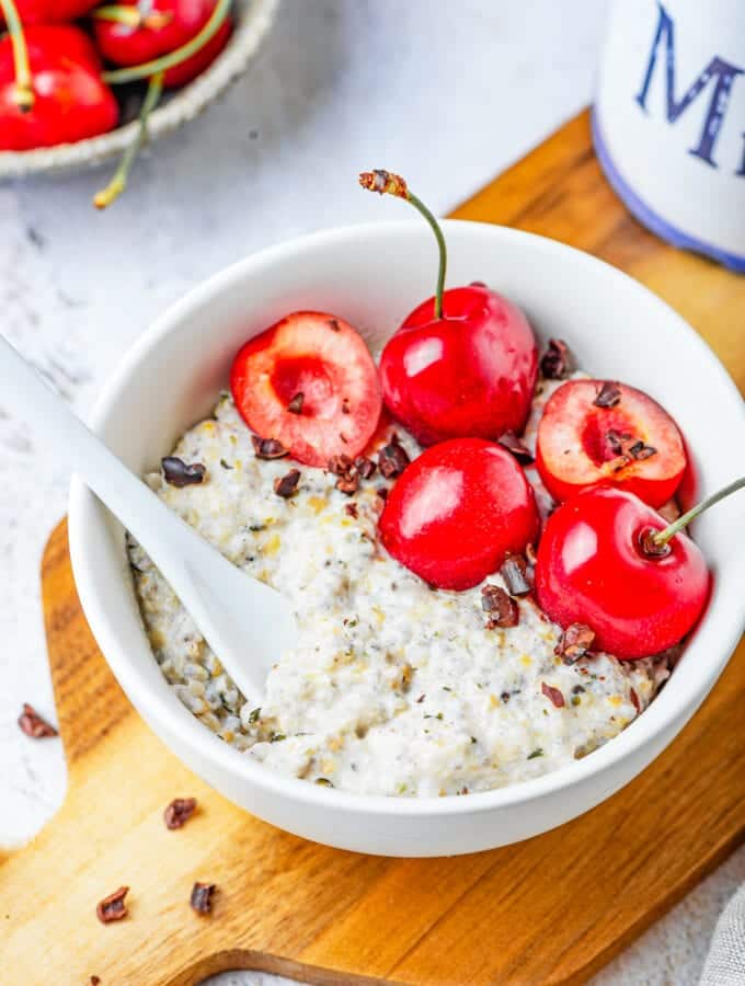 A white bowl filled with oatmeal, low carb chocolate, and a few cherries on a wooden cutting board.