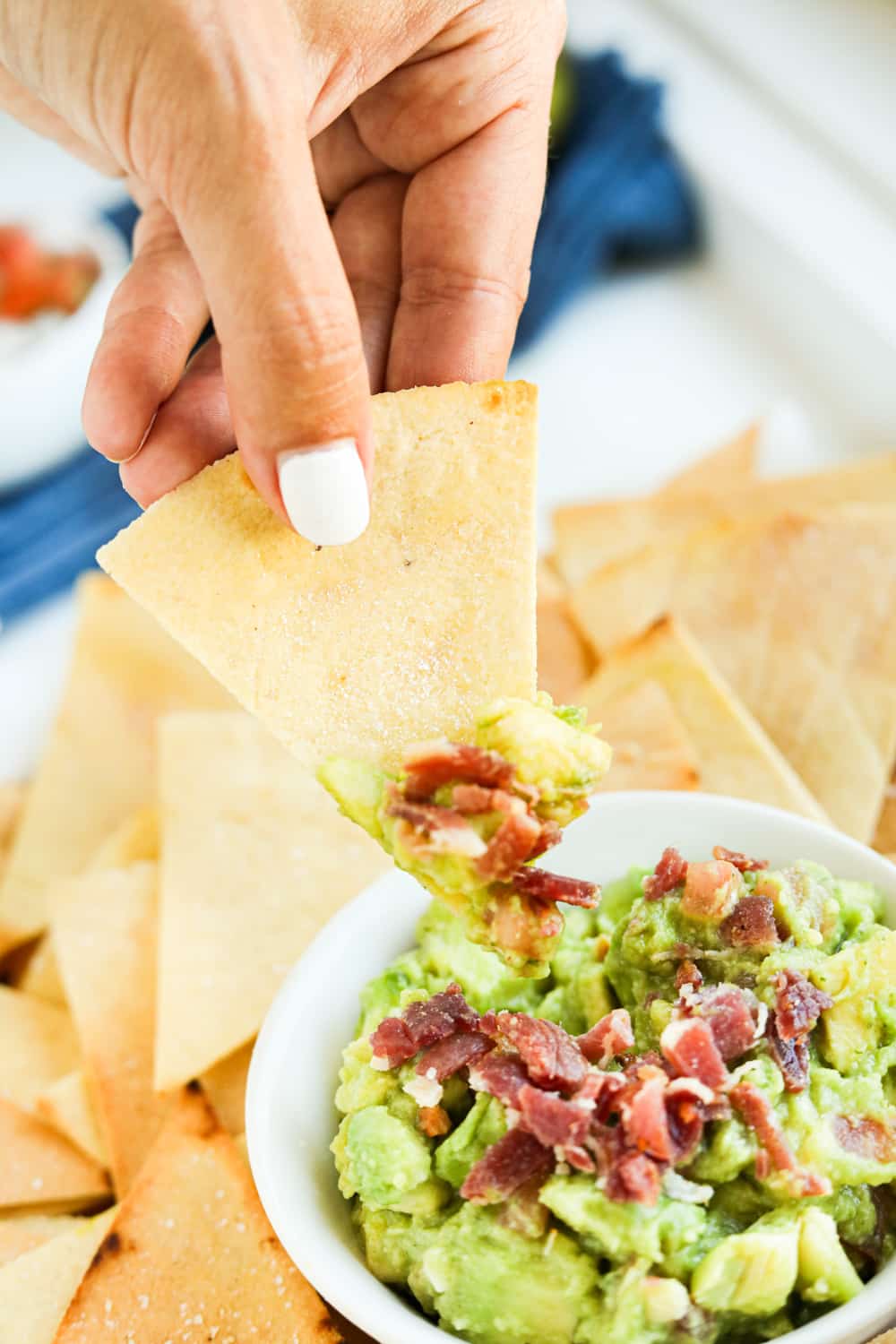 A tortilla chip scooping guacamole out of a bowl.