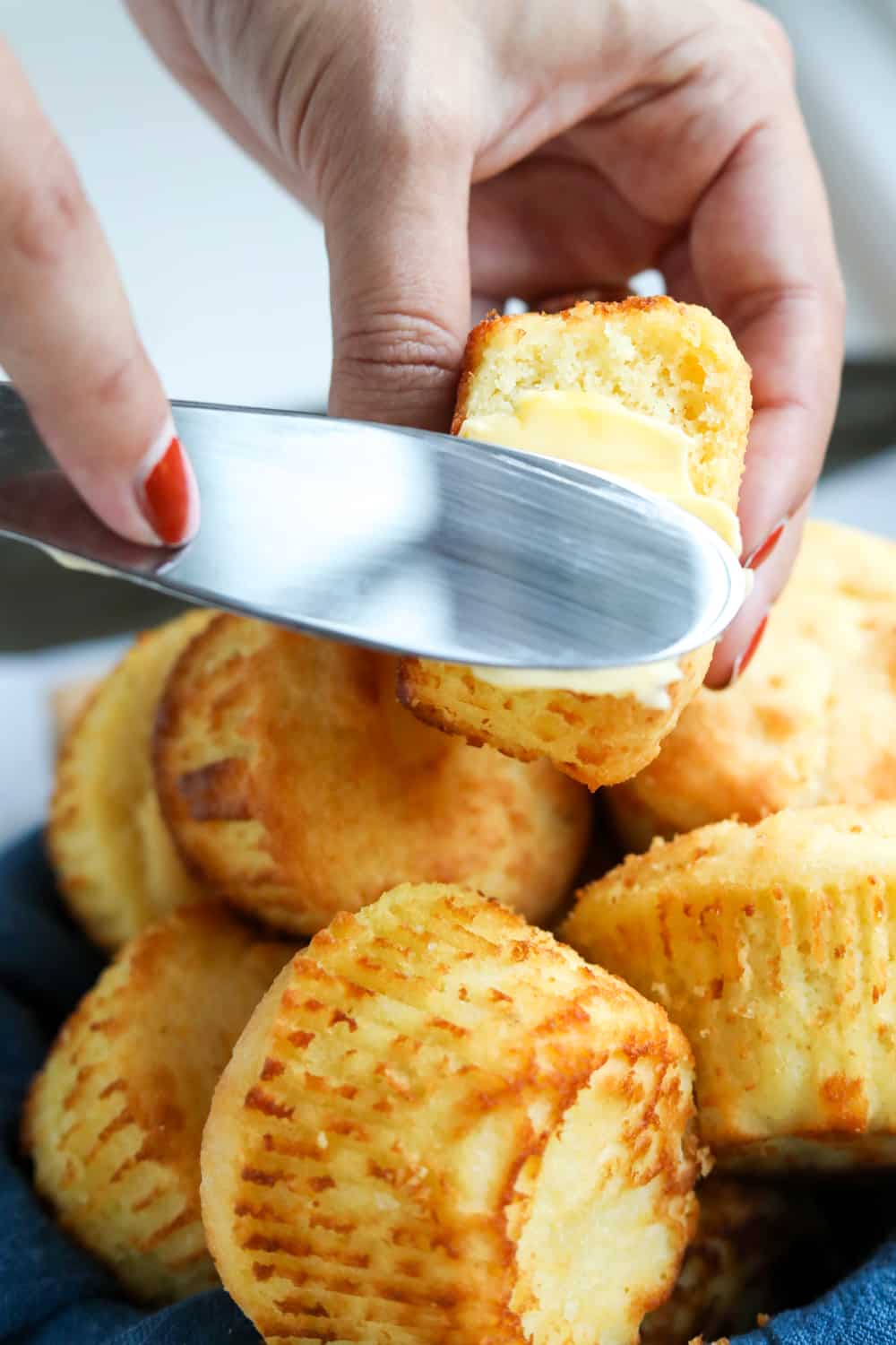 Butter being spread on a biscuit with a bite taken out of it.