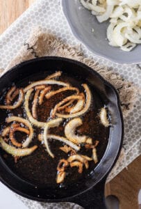 Slices of onions being fried in a cast iron pan.