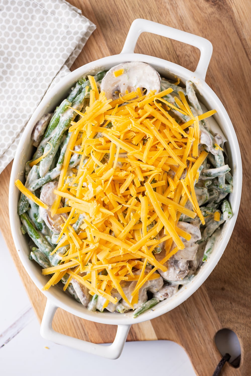 Green beans and mushrooms covered in a white sauce and topped with cheese in a white casserole dish.