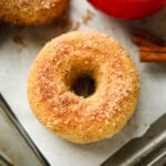 A donut on a baking sheet lined with parchment paper, and an apple next to it.