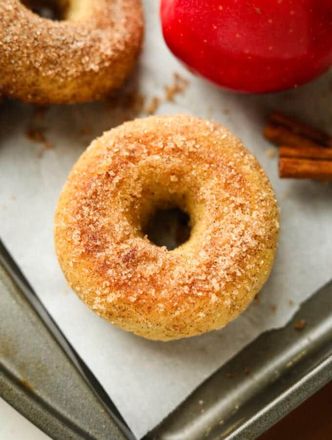 A donut on a baking sheet lined with parchment paper, and an apple next to it.