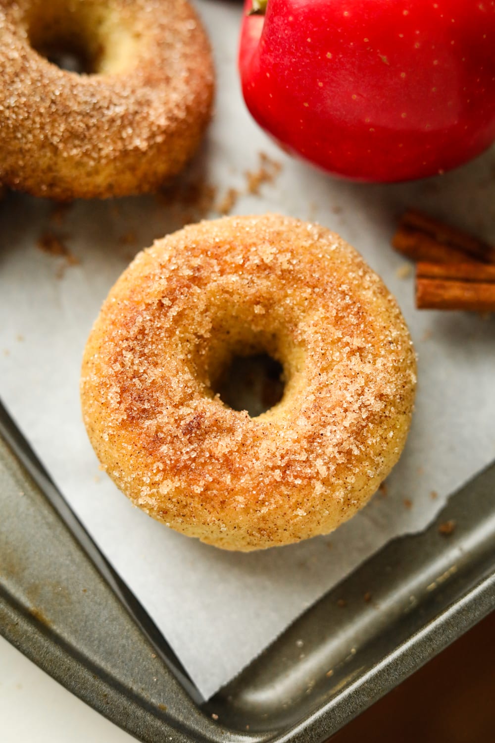 A donut on a baking sheet lined with parchment paper, and an apple next to it.