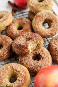 Donuts on a wire rack next to an apple.