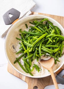 Green beans on top of mushrooms and a white sauce in a pot on top of a cutting board.