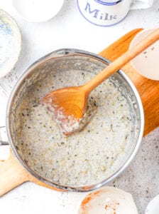 Oatmeal and a wooden spatula in a pot on a cutting board.