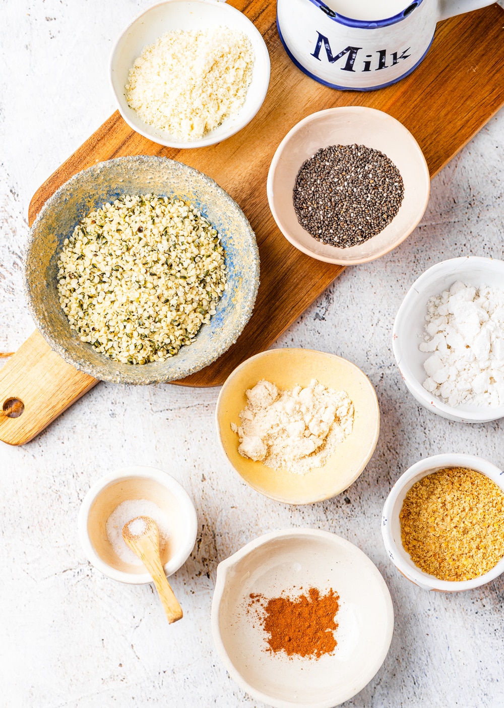 Small dishes filled with a variety of ingredients on a white table and a wooden cutting board.