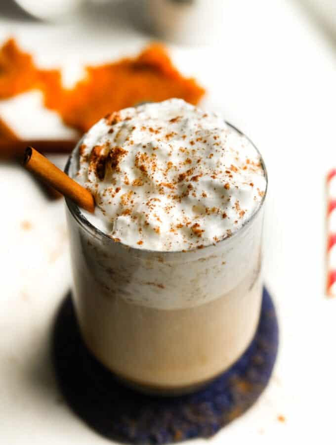 A clear glass cup filled with a pumpkin spice latte that's been topped with whipped cream and spices.