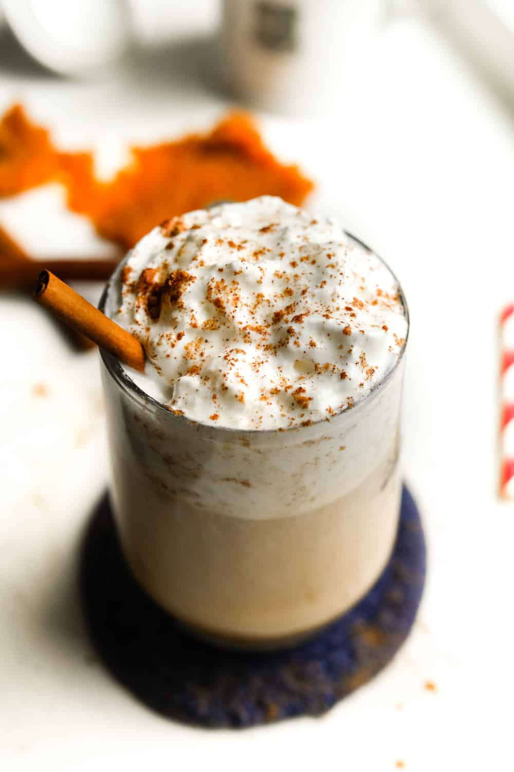 A clear glass cup filled with a pumpkin spice latte that's been topped with whipped cream and spices.