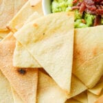 Tortilla chips pilled on top of one another next to a white bowl filled with guacamole.