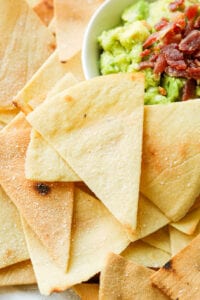 Tortilla chips pilled on top of one another next to a white bowl filled with guacamole.