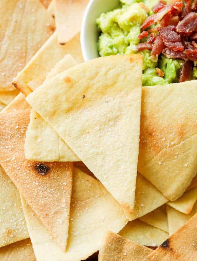 Tortilla chips pilled on top of one another next to a white bowl filled with guacamole.