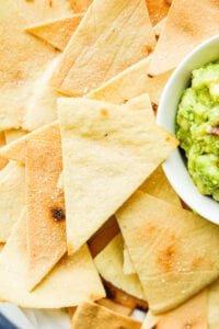 A pile of tortilla chips next to guacamole.