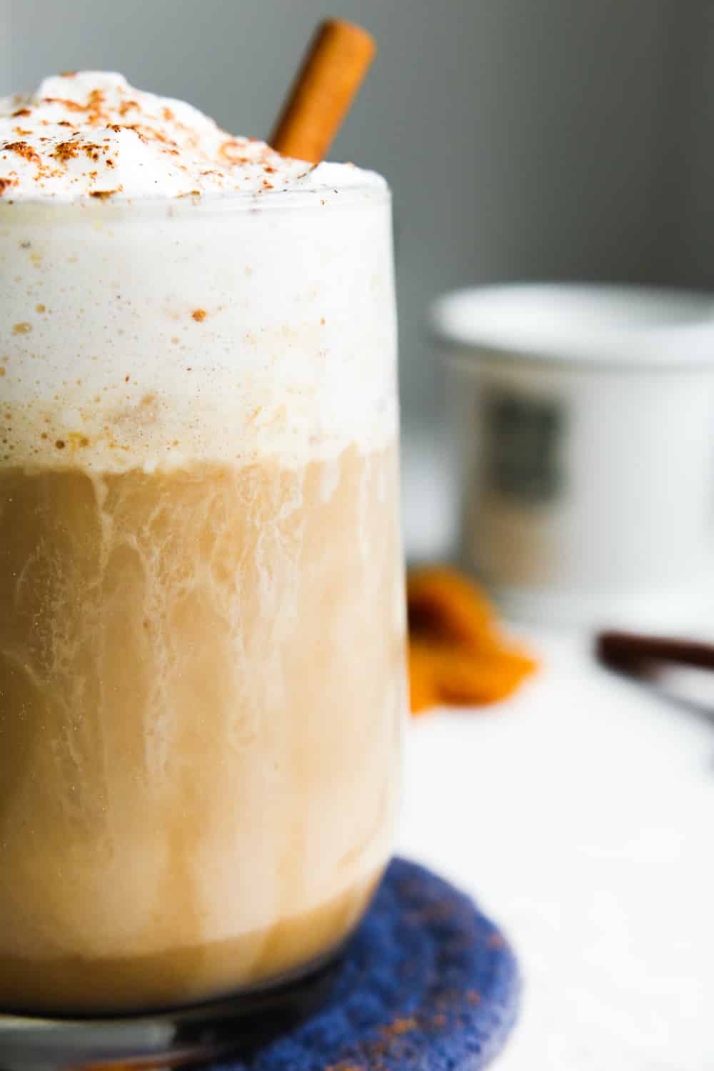 A pumpkin spice latte in a clear glass topped with whipped cream and set on a blue coaster.