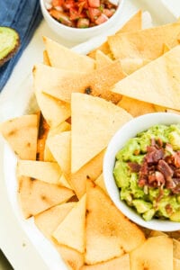 Tortilla chips on a plate next to a bowl of guacamole.